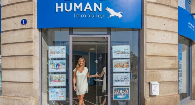 Portrait d’une agente immobilière souriante devant son agence Human