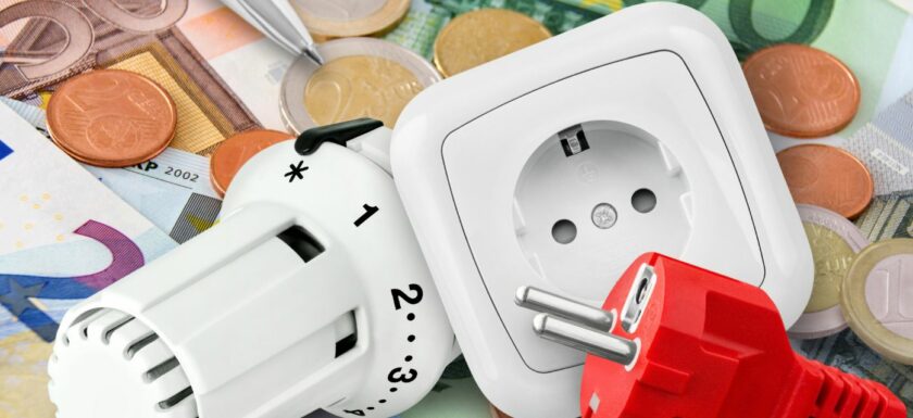 thermostat, prise électrique et fiche rouge poses sur des billets et pieces d’euros.