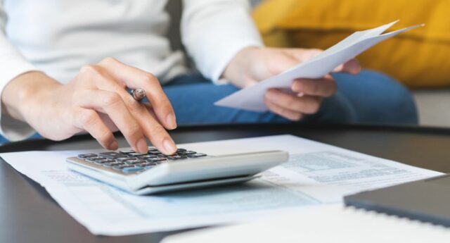 personne tenant un avis de taxe fonciere dans une main et la calculatrice dans l'autre