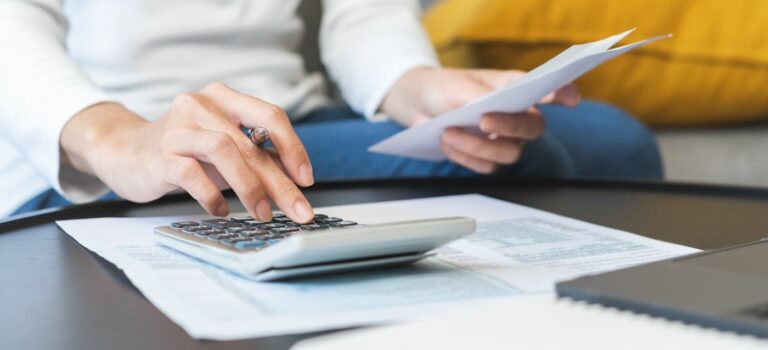 personne tenant un avis de taxe fonciere dans une main et la calculatrice dans l'autre