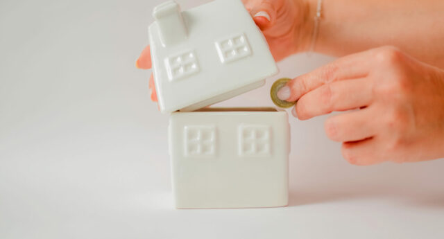 main deposant des euros dans un tirelire en forme de maison pour illustrer l'epargne logement