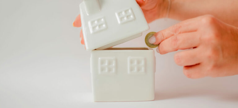 main deposant des euros dans un tirelire en forme de maison pour illustrer l'epargne logement