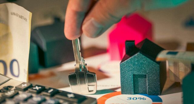 Main tenant une cle devant une maison miniature et une calculatrice pour illustrer le credit immobilier