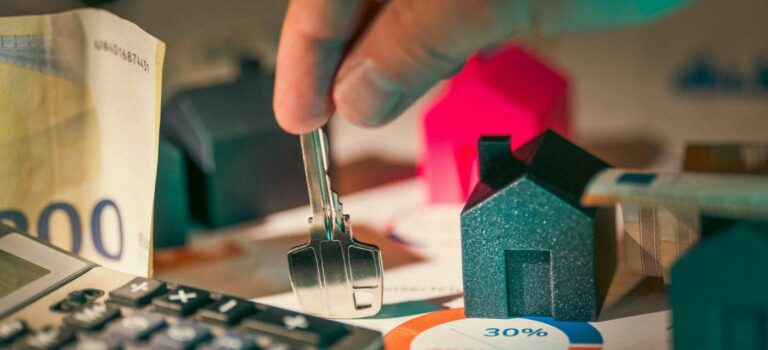 Main tenant une cle devant une maison miniature et une calculatrice pour illustrer le credit immobilier