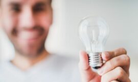 Homme souriant tenant une ampoule electrique dans sa main