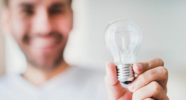 Homme souriant tenant une ampoule electrique dans sa main