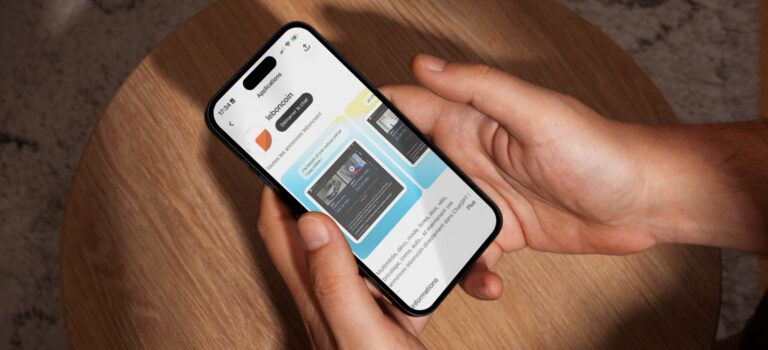 Ecran d'un iPhone 15 Pro Max tenu au-dessus d'une table en bois, affichant l'application leboncoin dans chatgpt
