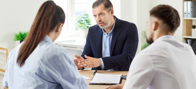 Agent immobilier expliquant a un couple de vendeurs pourquoi la hausse des taux impose d’ajuster le prix de vente