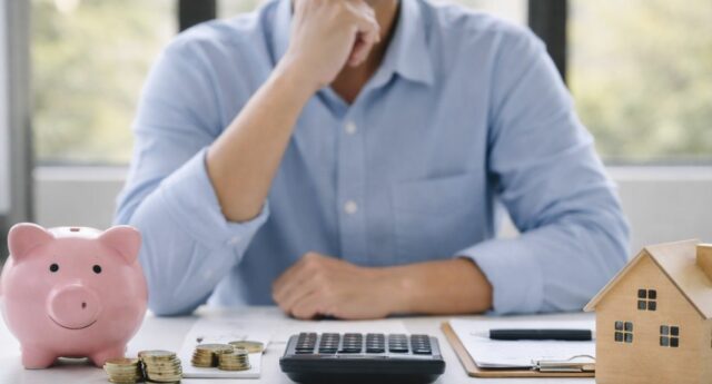 Personne comparant epargne et credit pour financer un projet immobilier avec calculatrice et modele de maison