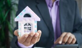 Investisseur immobilier tenant une maison miniature pour illustrer la gestion des charges et de la tresorerie locative.