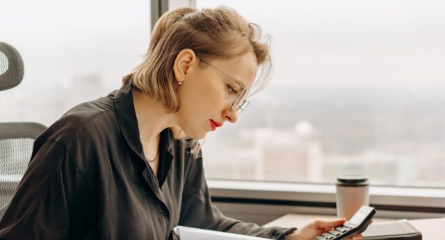 Femme faisant des comptes à son bureau, une calculatrice à la main