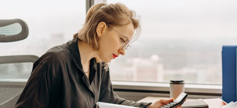Femme faisant des comptes à son bureau, une calculatrice à la main