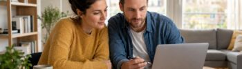 Un couple compare des offres d’assurance habitation sur ordinateur avec des documents, des cles et une loupe