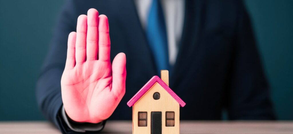 Agent immobilier refusant un mandat de vente represente par un geste de la main devant une maison
