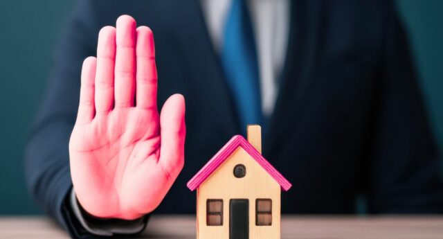 Agent immobilier refusant un mandat de vente represente par un geste de la main devant une maison