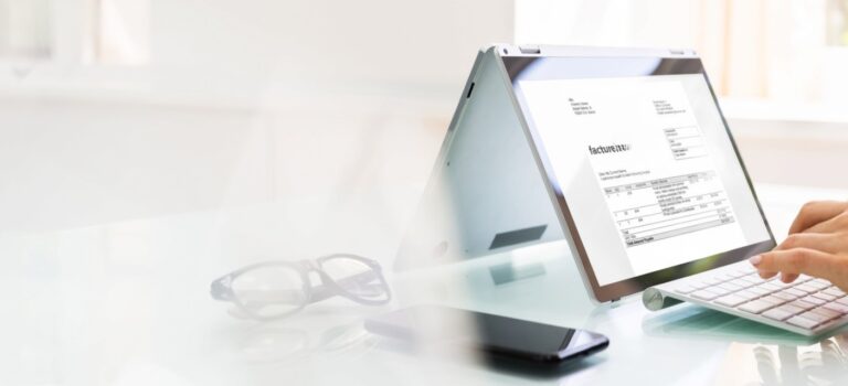 Professionnel saisissant des factures sur un ordinateur portable, entouré de documents comptables et d'une calculatrice.
