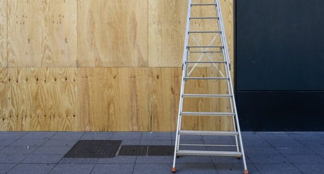Vitrine de commerce condamnée par des panneaux de contreplaqué après des émeutes, un escabeau posé devant