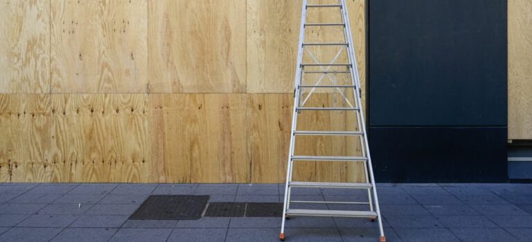 Vitrine de commerce condamnée par des panneaux de contreplaqué après des émeutes, un escabeau posé devant