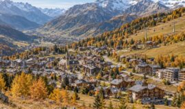 Vue panoramique d’un village de montagne en automne, avec chalets, résidences et télécabines sous des sommets enneigés