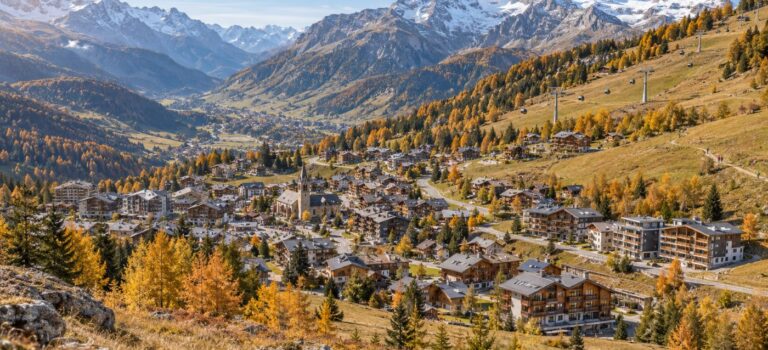 Vue panoramique d’un village de montagne en automne, avec chalets, résidences et télécabines sous des sommets enneigés
