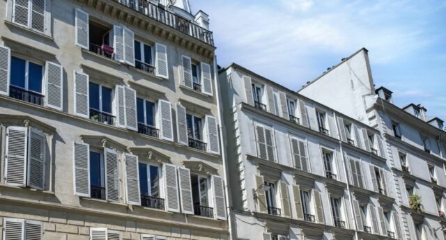 açade d’un immeuble ancien à plusieurs étages avec toiture en ardoise sous un ciel bleu nuageux