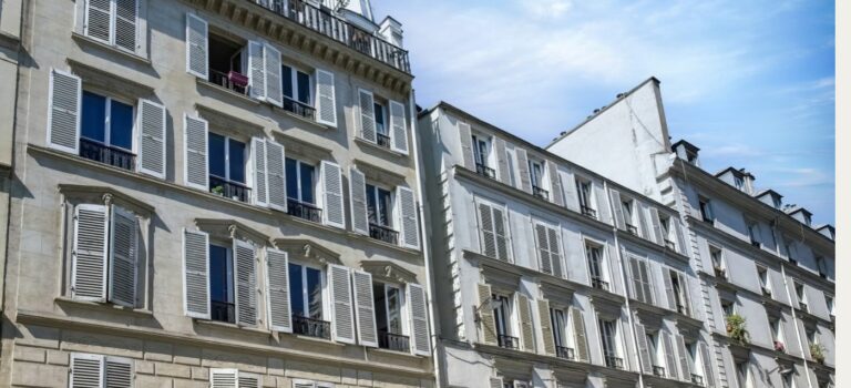 açade d’un immeuble ancien à plusieurs étages avec toiture en ardoise sous un ciel bleu nuageux