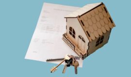 Maison miniature en bois posée sur un document de financement immobilier, avec un trousseau de clés au premier plan.