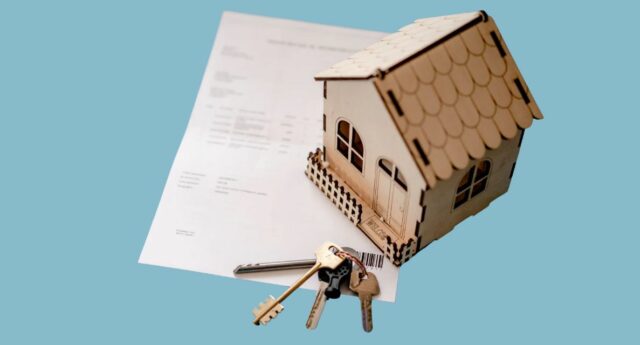 Maison miniature en bois posée sur un document de financement immobilier, avec un trousseau de clés au premier plan.