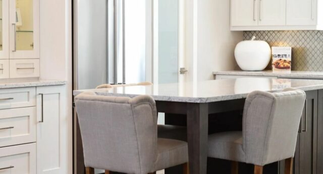 Cuisine moderne avec meubles blancs, îlot central et rangements gris, pour illustrer la valorisation d'un logement avant sa vente.